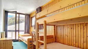 Habitación con literas, escritorio y silla, ventana con cortinas y vista al exterior.