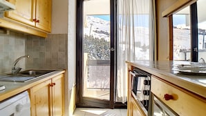 Una cocina con armarios de madera, un lavamanos y una ventana con vistas a una montaña nevada.