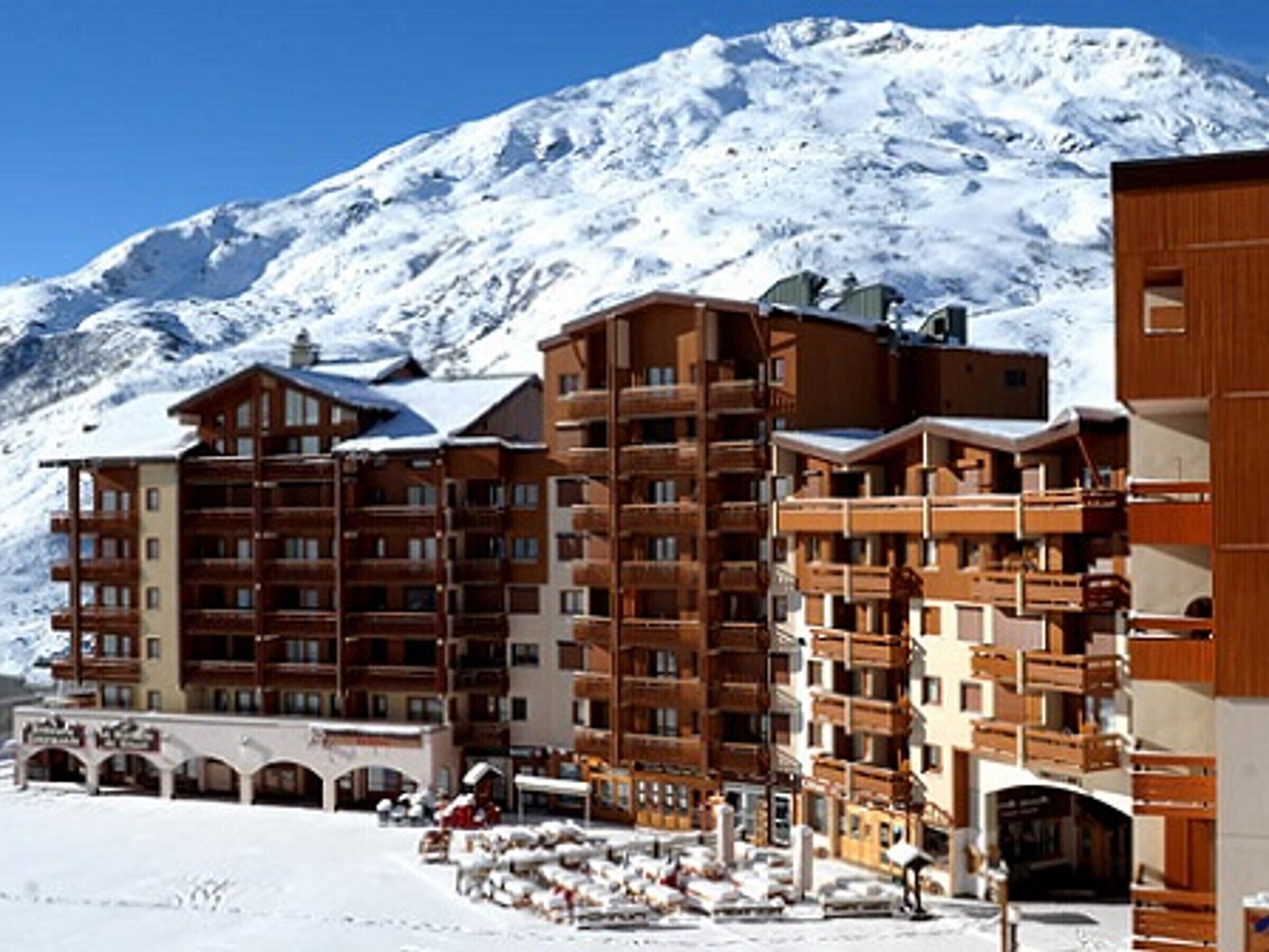 Un hôtel à plusieurs étages, doté de balcons en bois, avec une piste de ski en arrière-plan.