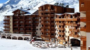 Um hotel com vários andares, varandas de madeira e uma montanha coberta de neve ao fundo.