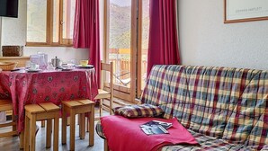 Um quarto aconchegante com uma mesa de jantar posta para dois, um sofá xadrez e uma janela com cortinas.