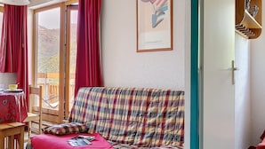 Um quarto aconchegante com sofá xadrez, mesa de jantar com cadeiras e uma janela grande com cortinas vermelhas.