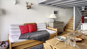 A cozy living room with a sofa, a dining table, and a staircase leading to an upper level.