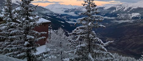 A mountain view with snow-covered trees and a building in the foreground.