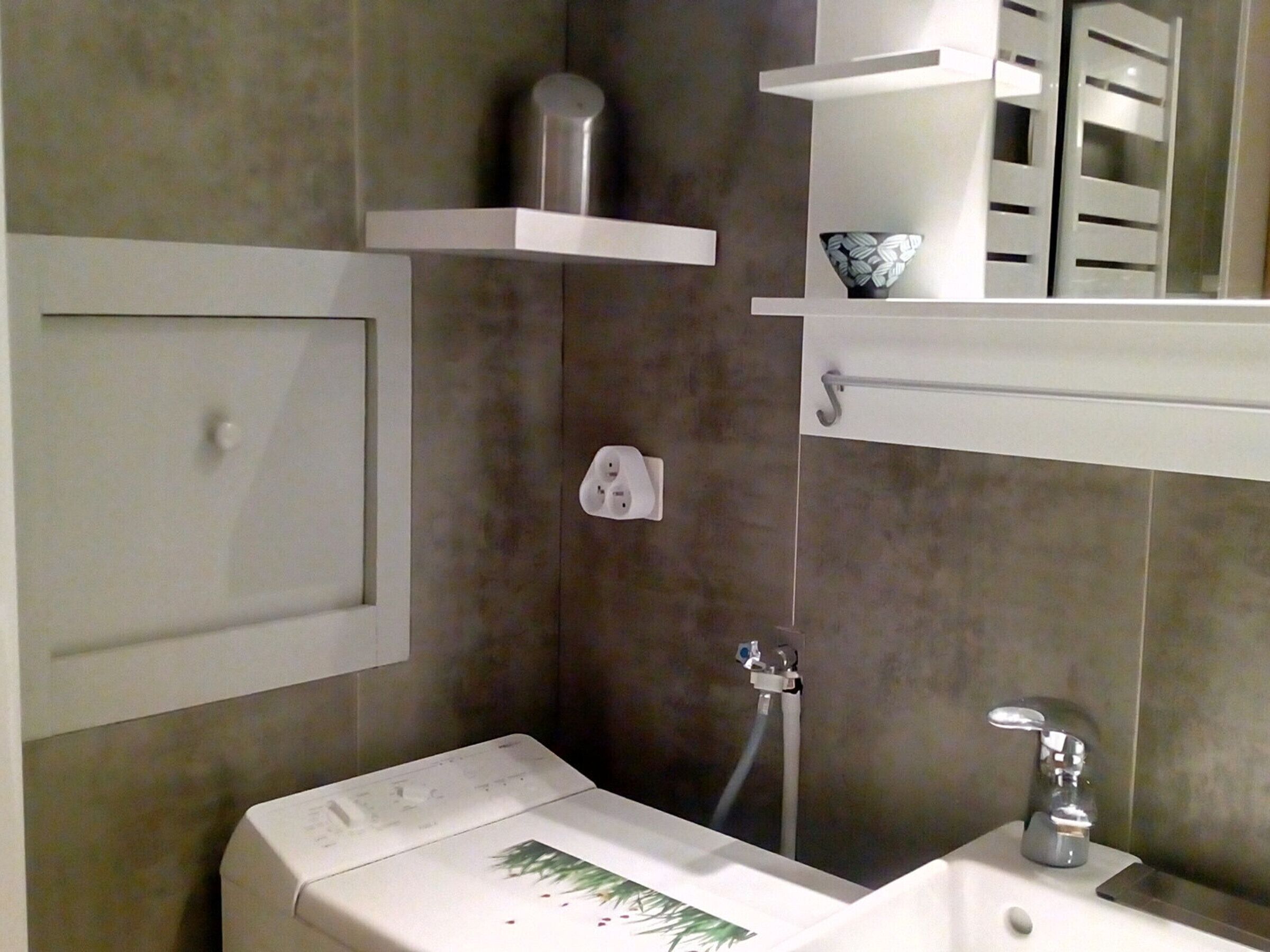 Ein Badezimmer mit weißem Waschbecken, einem Spiegel, einem Handtuchhalter und einer Dusche.
