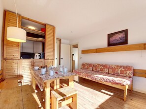 Una habitación acogedora con una mesa de comedor de madera preparada para cuatro personas, un sofá y una cocina con armarios de madera y una lámpara colgante.