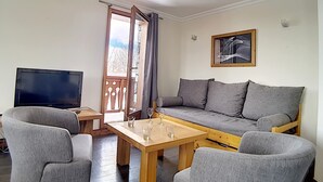 A living room with a sofa, two armchairs, a wooden coffee table, and a TV.