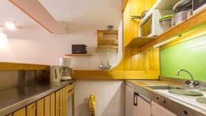 A compact kitchen with wooden cabinets, a built-in oven, a coffee maker, and a green backsplash. - 2-Room Apartment · Balcony · Free Wifi (Les Arcs 1800)