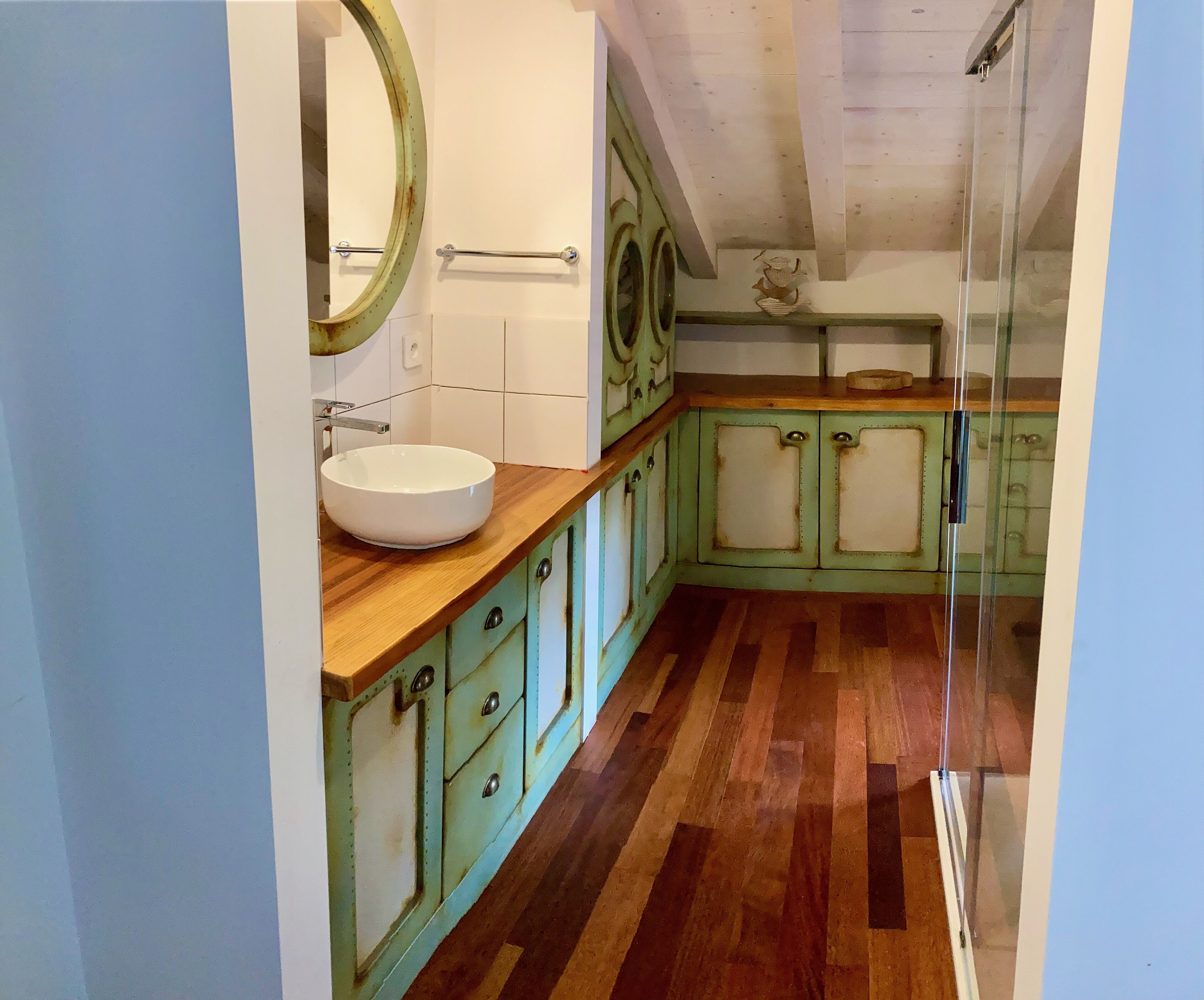 Un baño con tocador de madera, un lavamanos blanco y armarios verdes.