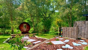 Eine Holzhütte mit einer runden Tür, umgeben von einem Garten mit trittfesten Steinen und einem Holzzaun.