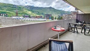 A balcony with a table and chairs, a view of mountains, and buildings in the background. - Central apartment with balcony for 6 people (Les Menuires)