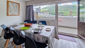 A dining area with a table set for two, a view of a mountainous landscape, and a window with a view of a building and a tower. - Central apartment with balcony for 6 people (Les Menuires)