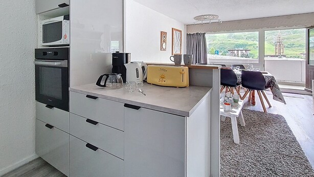 A modern kitchen with a microwave, coffee maker, toaster, and a dining area with a table and chairs. - Central apartment with balcony for 6 people (Les Menuires)