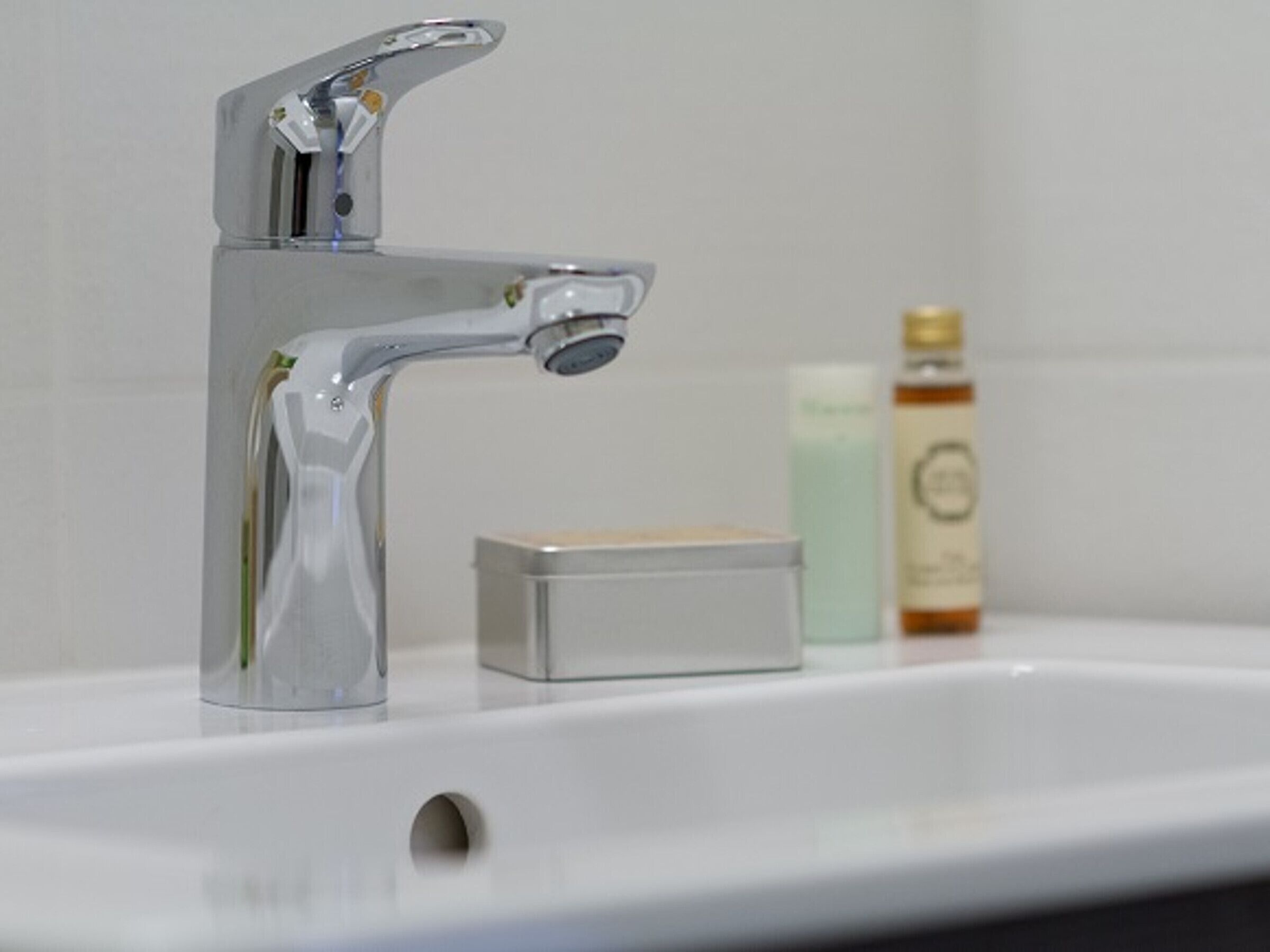 A bathroom sink with a chrome faucet, a soap dispenser, and a bottle of liquid soap.
