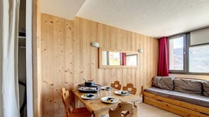 Un coin repas en bois, avec une table, des chaises et une fenêtre ornée d’un rideau rouge.