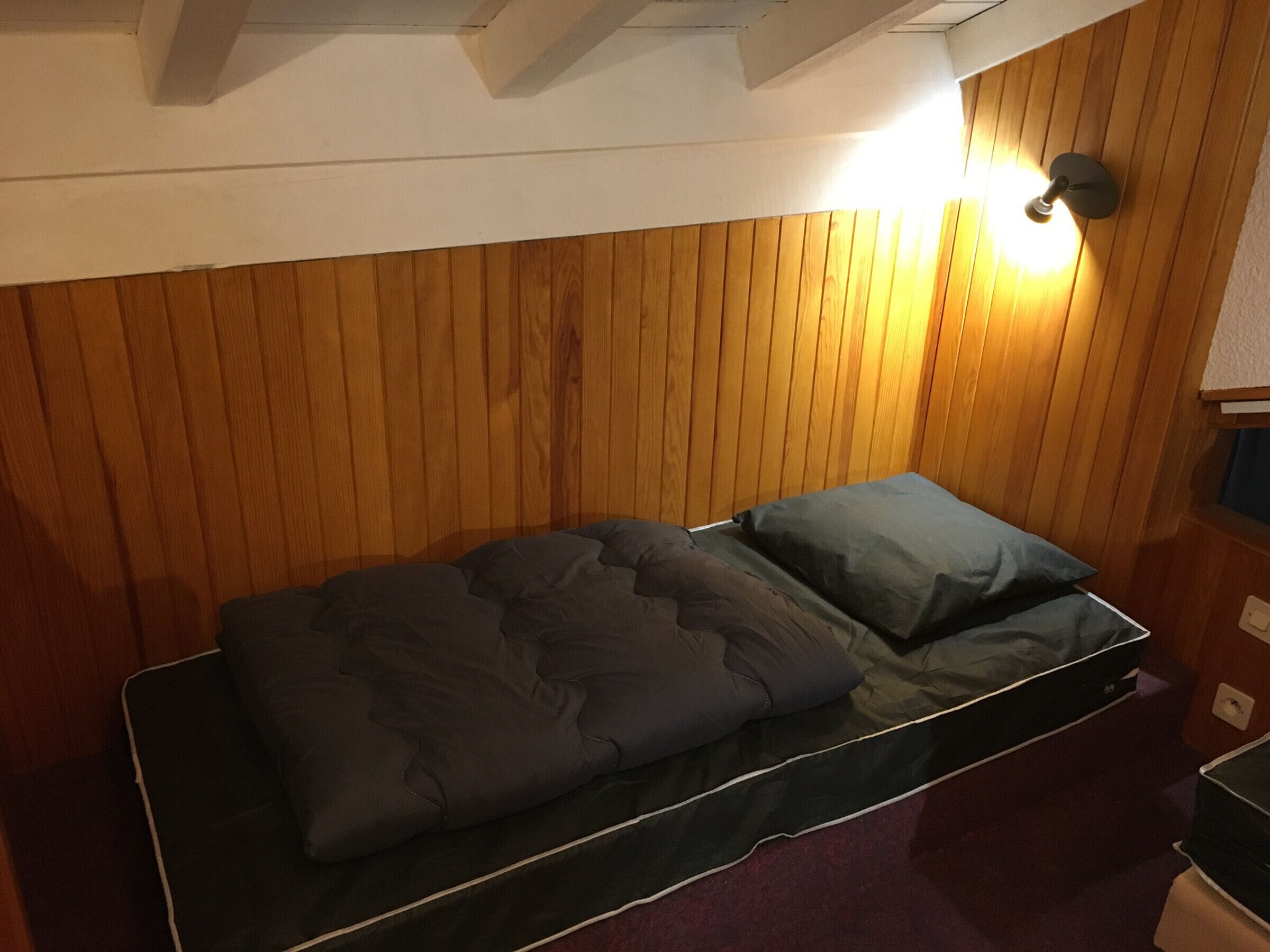 Una habitación pequeña con una cama individual, paneles de madera y una lámpara en el techo.