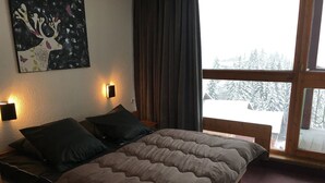 Une chambre à coucher avec un lit, deux lampes de chevet, un tableau au mur et une fenêtre donnant sur des arbres couverts de neige.