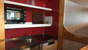 Une cuisine compacte équipée d’un four à micro-ondes, d’un grille-pain et d’un lave-vaisselle, avec des murs rouges et des meubles en bois.