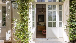 A white building with a front door, a chandelier, and a bench inside. - The Arbour, by Veeve (Paris)