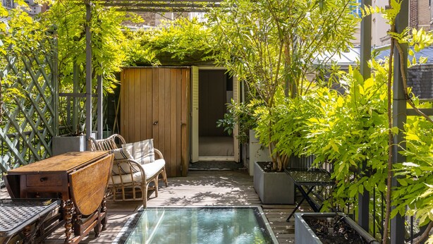 A sunlit patio with a wooden table and chairs, a small pool, and lush greenery. - The Arbour, by Veeve (Paris)
