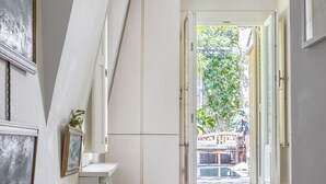 A bedroom with a bed, a bedside table, a mirror, and a view of the outside. - The Arbour, by Veeve (Paris)