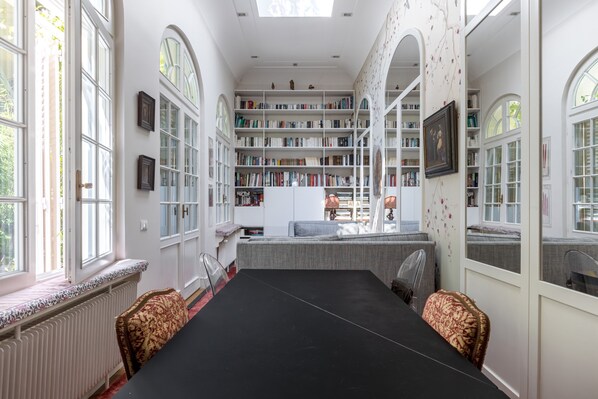 A spacious library with high ceilings, large windows, and a central black table.