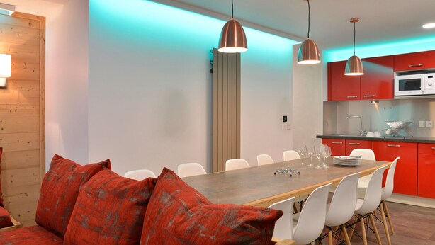 Una cocina moderna con armarios rojos, una mesa de comedor de madera y sillas blancas.