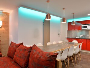 A modern kitchen with red cabinets, a wooden dining table, and white chairs.