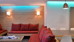 Una habitación moderna con pared de madera, sofá rojo estampado, sillas blancas, una mesa de madera y dos luces adosadas a la pared.