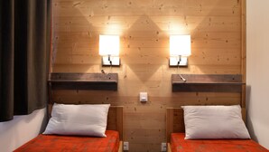 Una habitación con dos camas, cada una con una colcha roja y almohadas blancas, cabeceras de madera y luces fijadas a la pared.
