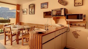A compact kitchen with a wooden island, a dining table with chairs, and a view of the outdoors. - Bright studio in Les Menuires, ski-in/ski-out, balcony (Les Menuires)