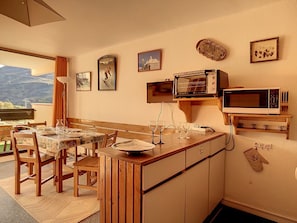 Une cuisine compacte avec un îlot central en bois, une table à manger avec des chaises et une vue sur l’extérieur.
