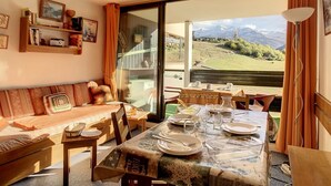 A cozy room with a dining table set for four, a sofa, and a large window offering a mountain view. - Bright studio in Les Menuires, ski-in/ski-out, balcony (Les Menuires)