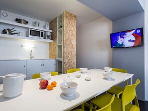 Un espace repas moderne avec une table blanche, des chaises jaunes et un téléviseur fixé au mur.