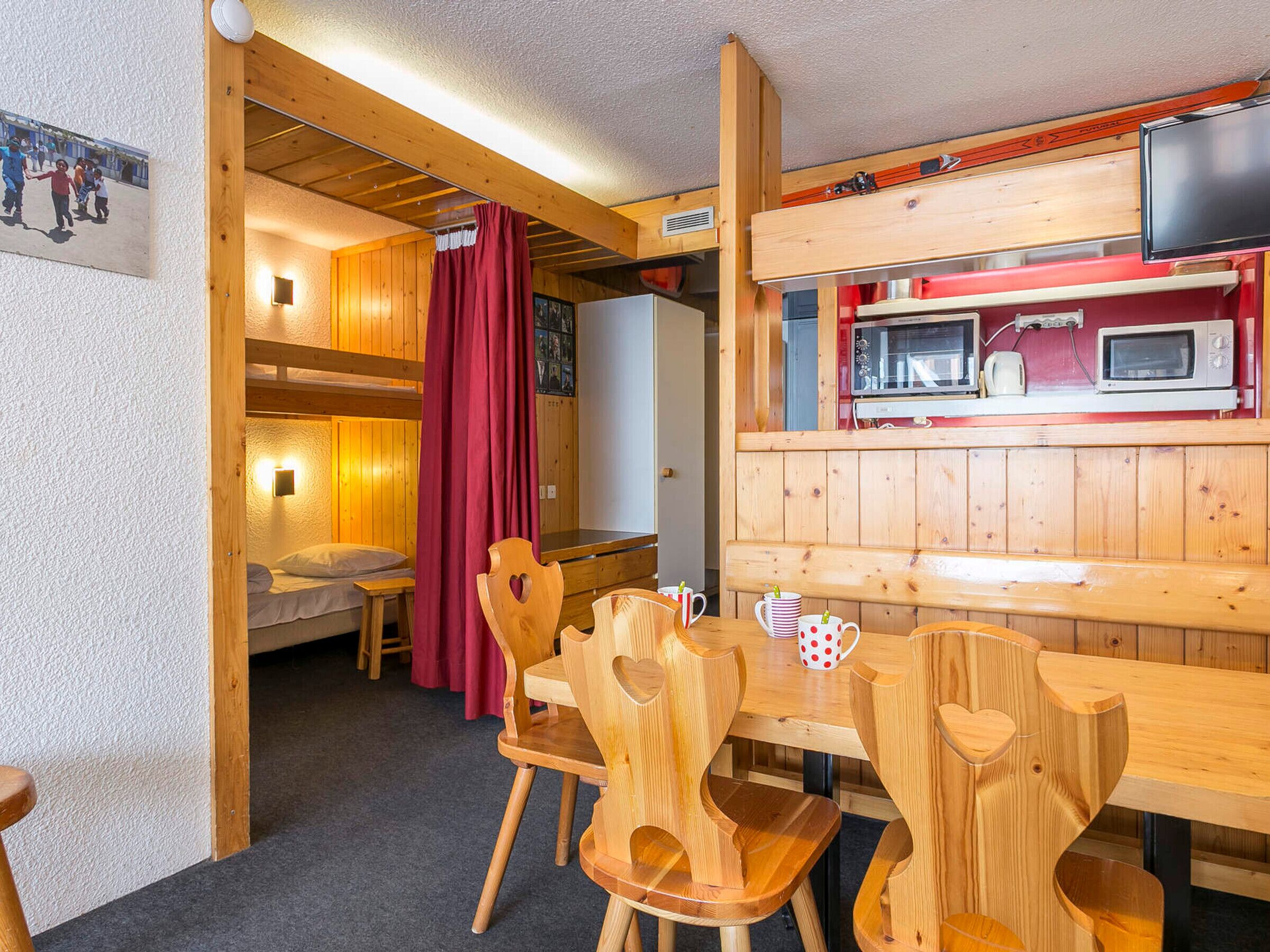 Une cabane en bois chaleureuse comprenant un coin repas, une cuisine équipée d’un four à micro-ondes et un espace nuit avec un lit superposé.