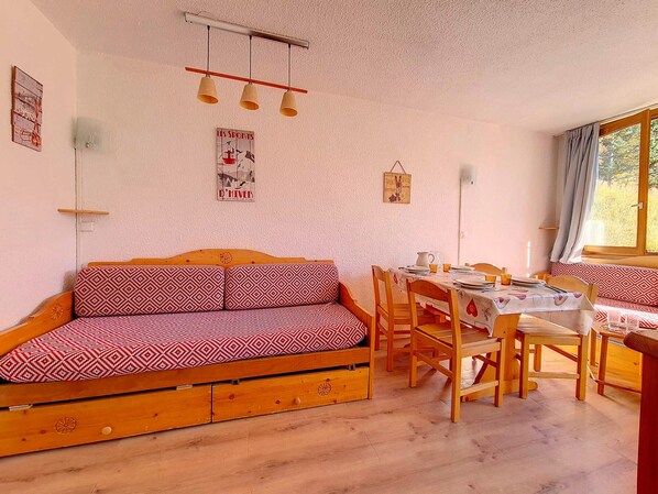 Una habitación acogedora con un sofá de madera, una mesa de comedor y sillas. Hay adornos en la pared y una ventana con cortinas.