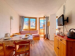 Una habitación acogedora con una mesa de comedor preparada para dos personas, un sofá, un televisor y una tetera sobre la encimera.