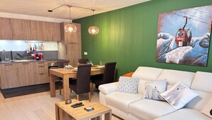 A modern living room with a dining area, a kitchen in the background, and a green accent wall. - Les Gets: 2-bed apartment with terrace and WIFI, near center and slopes (Les Gets)