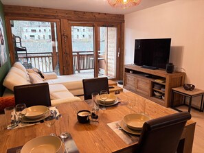 Un comedor con una mesa de madera dispuesta para cuatro personas, un sofá y un televisor.