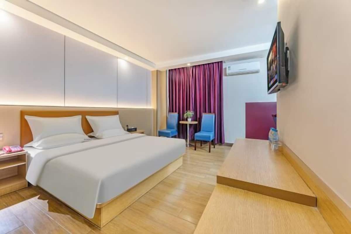 A hotel room with a bed, bedside table, chair, and a small table with a plant.