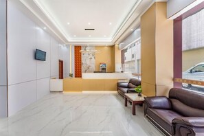 A modern hotel lobby with a reception desk, seating area, and a large window.