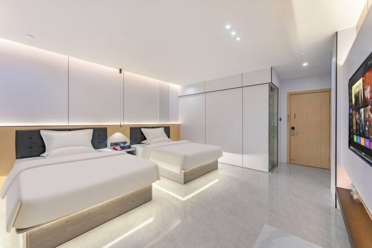 A modern hotel room with two beds, a large wardrobe, and a flat-screen TV.