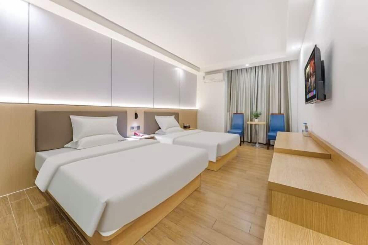 A hotel room with two beds, a desk, a TV, and a window with curtains.