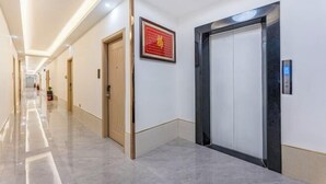 Un pasillo de hotel con piso de mármol, un cuadro en la pared y un ascensor.