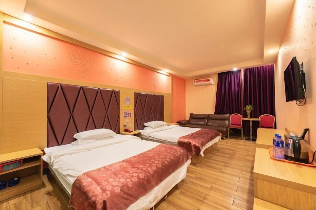 A hotel room with two beds, a desk, a chair, a TV, and a small table with a plant.