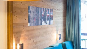 A room with a wooden wall, a blue sofa, a painting, and a window with curtains. - Renovated ski-in studio with balcony (Les Arcs 1800)