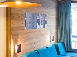 Een kamer met een houten wand, een blauwe bank, een schilderij en een raam met gordijnen.