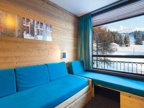 Une pièce avec un mur en bois, un canapé bleu et une fenêtre donnant sur des arbres et des montagnes enneigés.