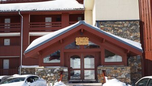 A snow-covered building with a stone facade and a wooden entrance. There are cars parked in front, and a sign above the entrance reads "LE NECOU".