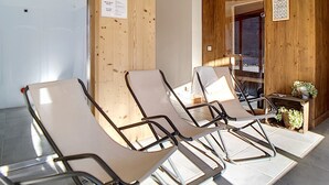 A waiting area with wooden panel walls, a small table with plants, and three reclining chairs.